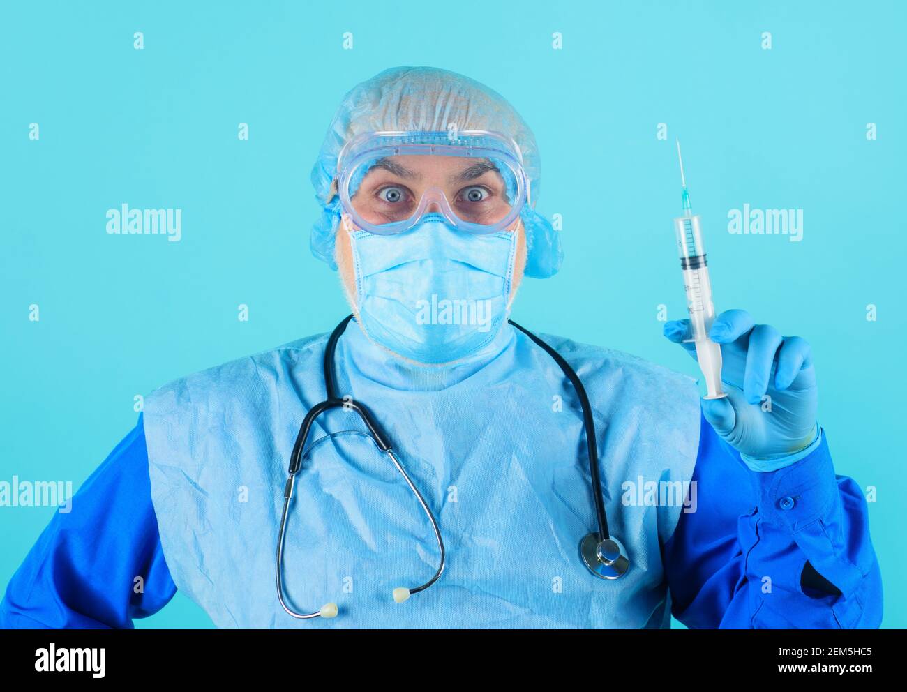 Medico in tuta protettiva, occhiali e maschera medica con siringa. Infermiere di sesso maschile che prepara l'iniezione con il vaccino. Foto Stock