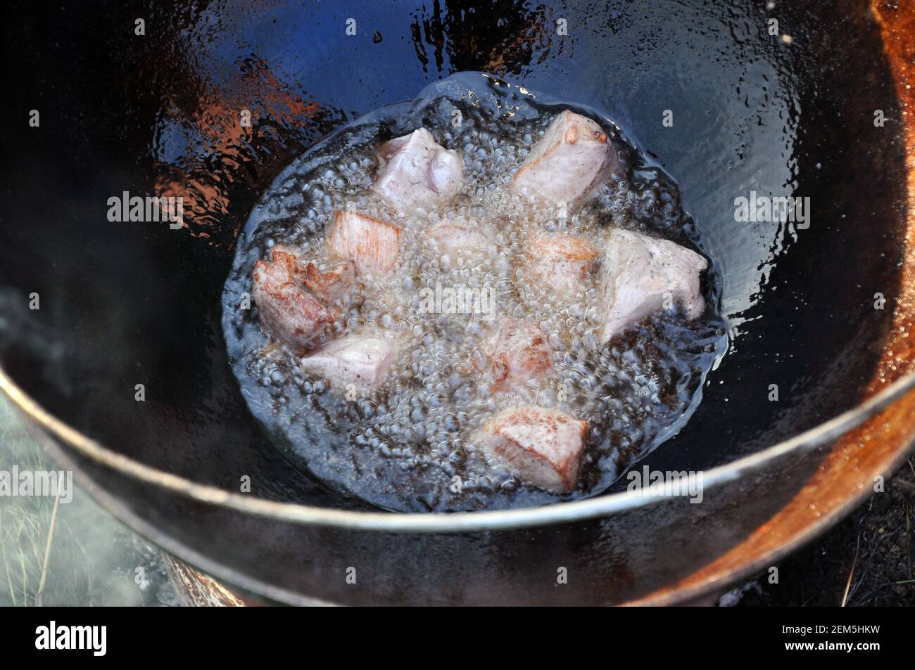 Friggere la carne in calderone all'aperto sul fuoco. Viaggi, turismo, cucina pic-nic, cucinare al palo in un calderone, fuoco e fumo. Foto Stock