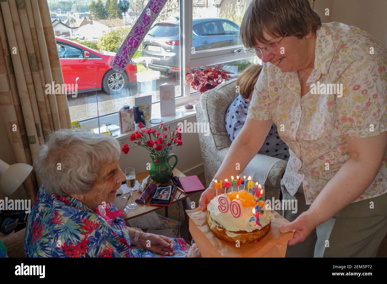 Donna che riceve la sua torta di compleanno 90 da sua figlia Foto Stock