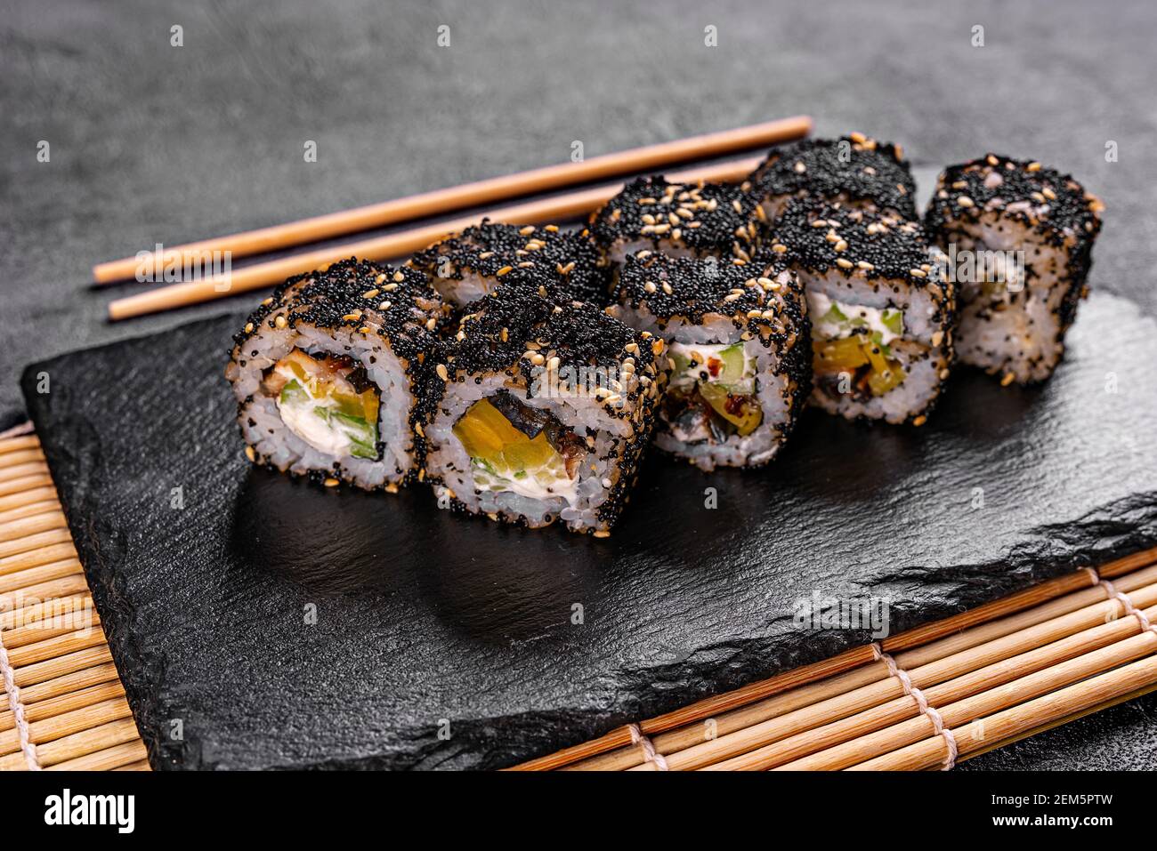 Rotolo di sushi con salmone, avocado e formaggio su un piatto di pietra nera su un piatto bianco. Menu sushi. Cibo giapponese, sushi di riso nero Foto Stock