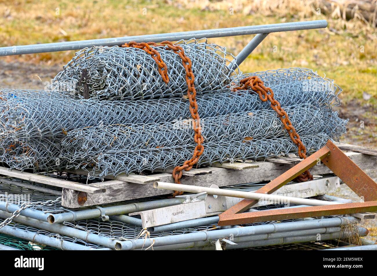 Una pila di recinzioni di maglie della catena arrotolate e scartate con una catena arrugginita. Foto Stock