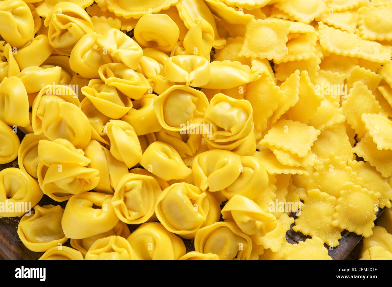 Tartollini con formaggio o carne per la cottura in brodo, forme diverse. Piatto tradizionale per celebrazioni in italia, regione Emilia Romagna. Pasta fresca fatta in casa con ripieno su un tavolo di legno. Foto Stock