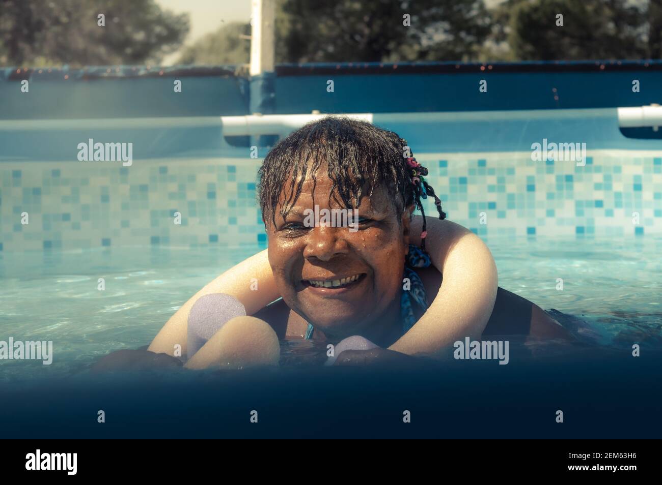 Allegra donna afroamericana sorridente che nuota in piscina una giornata di sole Foto Stock