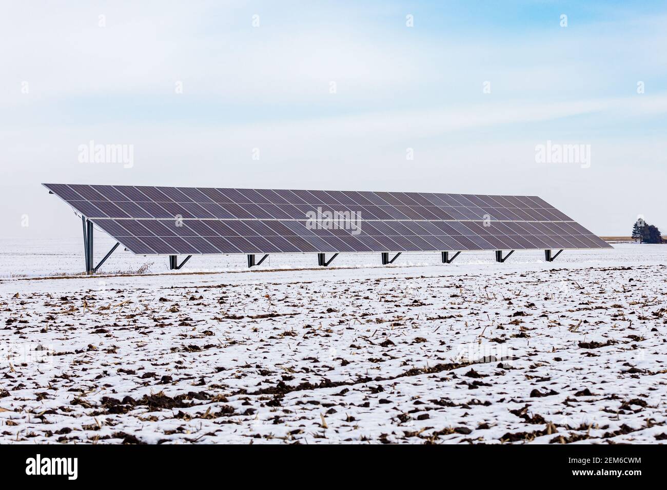 Pannelli solari montati a terra in campo agricolo coperto di neve in giornata nuvolosa. Concetto di energia rinnovabile, risparmio delle bollette di servizio e generazione di elettricità Foto Stock