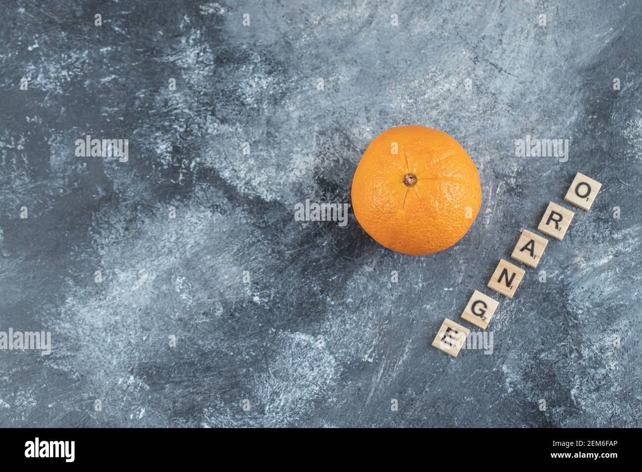 Frutto arancione intero con lettere in legno su sfondo marmoreo Foto Stock