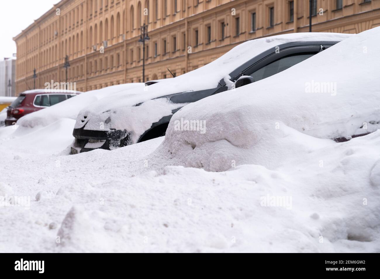 Auto parcheggiate coperte di neve su una strada innevata non pulita dopo la nevicata. Maltempo invernale Foto Stock
