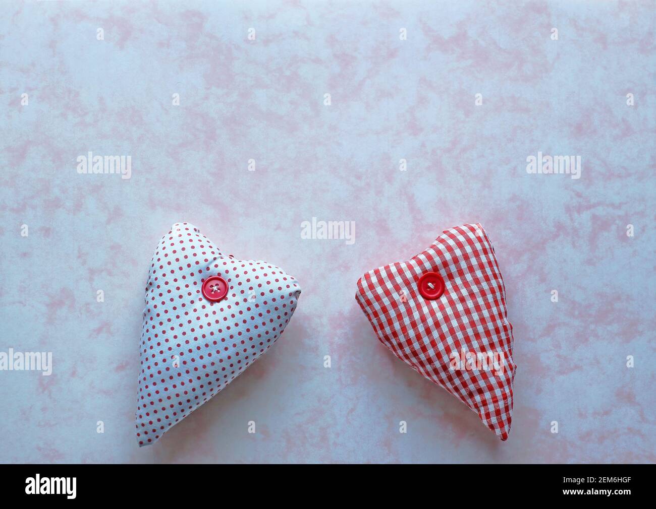 Due cuori in tessuto rosso e bianco su un marmo rosa sfondo della carta Foto Stock