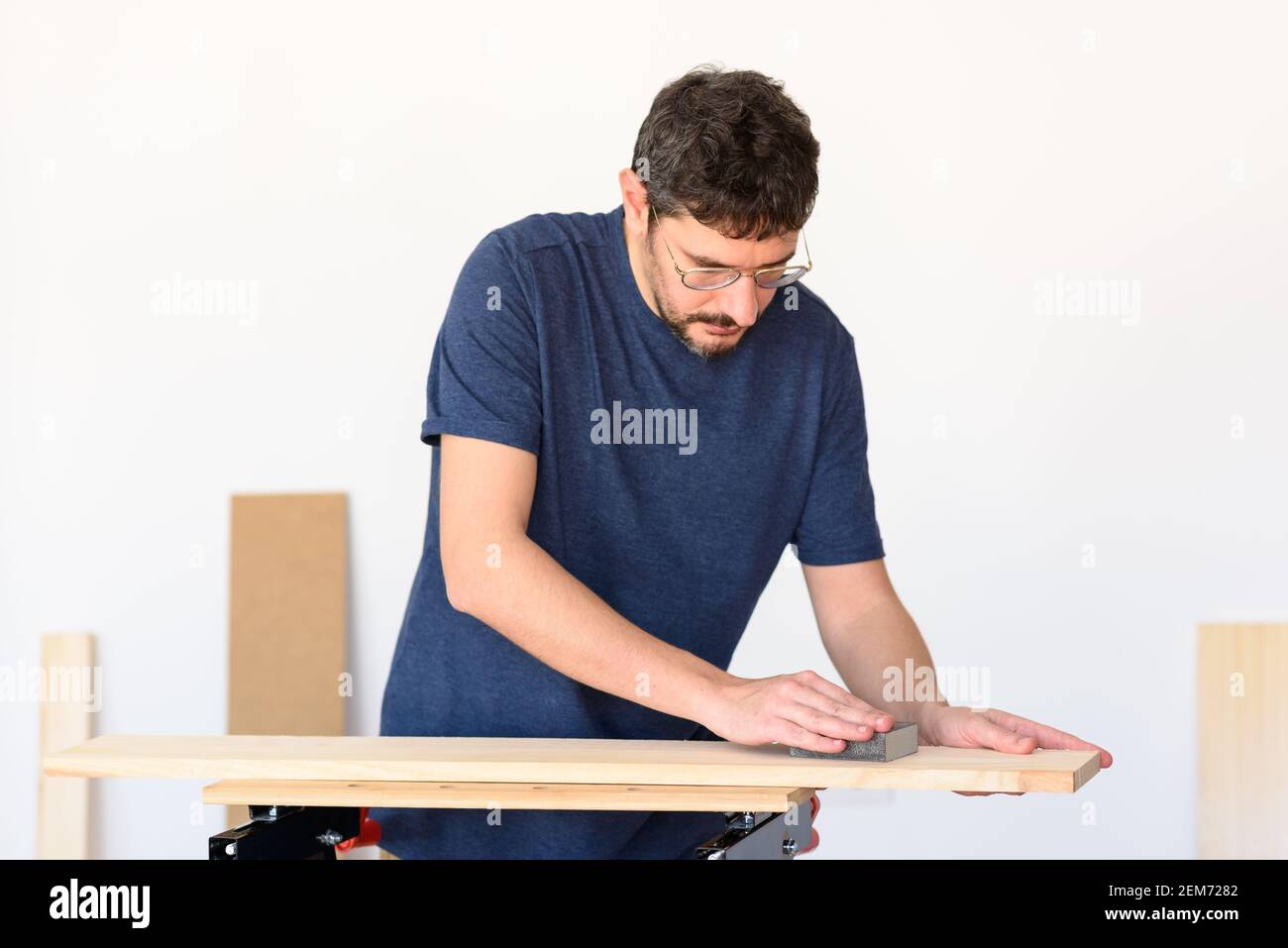 Uomo a casa levigando un legno su un banco da lavoro. Sfondo bianco. Foto Stock