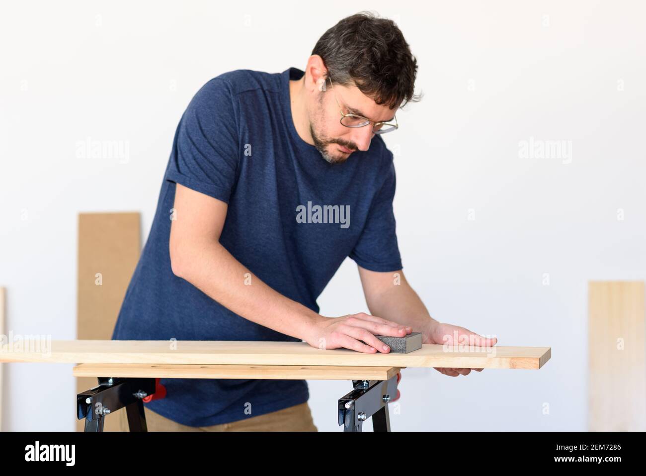 Uomo a casa levigando un legno su un banco da lavoro. Sfondo bianco. Foto Stock