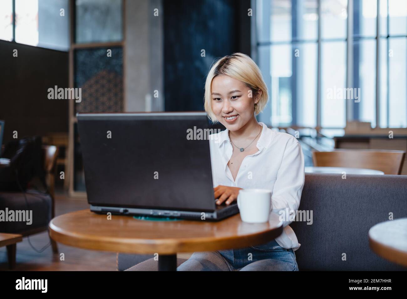 Giovane bella donna asiatica che lavora sul suo computer portatile in un bar, mentre beve caffè. Foto Stock