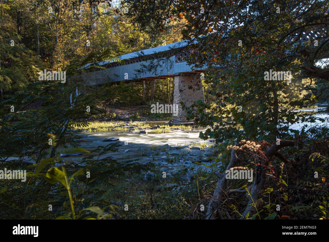 Cleveland, Alabama/USA-Ott 17, 2020: Lunga esposizione del panoramico Swann Covered Bridge retroilluminata dal sole tramontante visto attraverso una pausa nel tr Foto Stock