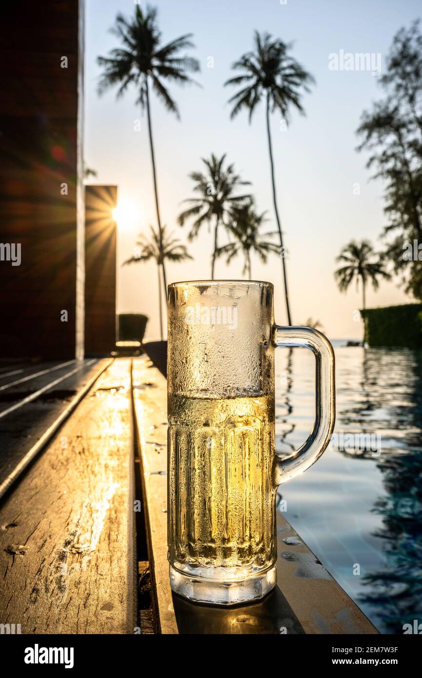 Alti bicchieri da birra con flauti disposti su una terrazza in legno vicino alla piscina presso la località balneare. Sfondo con palme da cocco, la sera il li dorato Foto Stock