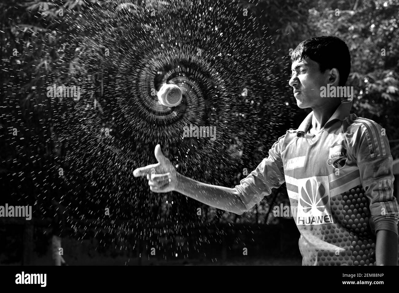 Cumilla, Bangladesh - 24 novembre 2017: Il ragazzo sta spruzzando acqua con una palla di cricket. Bianco e nero Foto Stock
