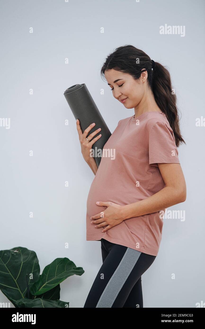 Donna incinta dolce al club di yoga, che posa per una foto con la mano sul ventre Foto Stock