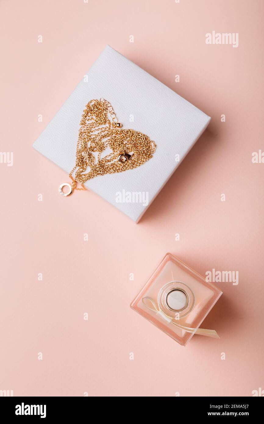 Un regalo per San Valentino. Profumo e una scatola con una catena d'oro su sfondo rosa. Foto Stock