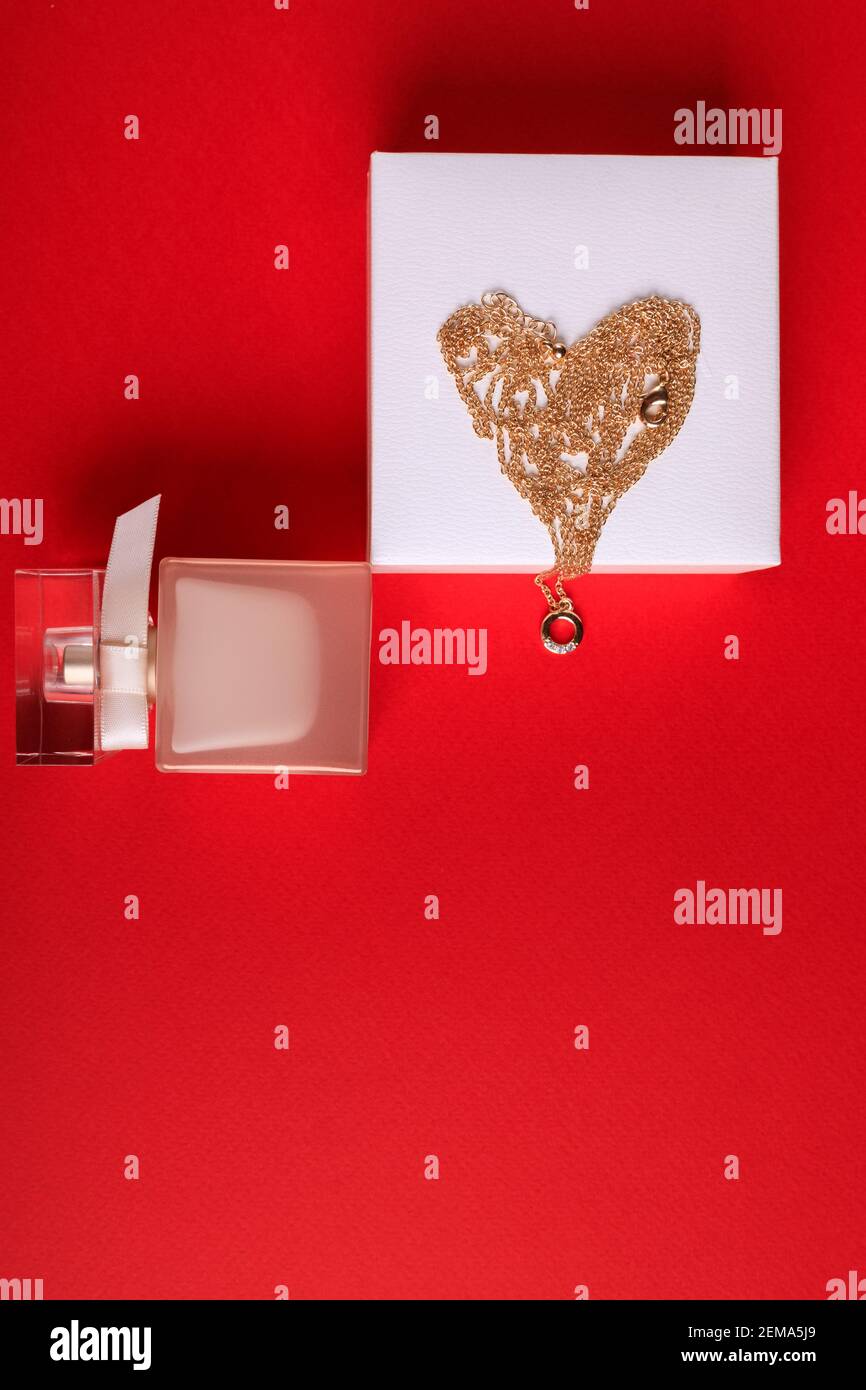 Un regalo per San Valentino. Profumo e una scatola con una catena d'oro su sfondo rosso. Foto Stock
