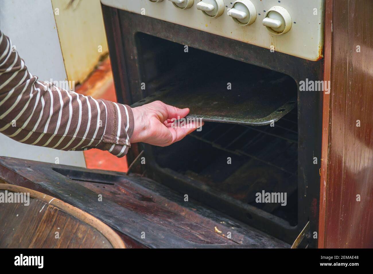 Una donna tira fuori una teglia dal forno di una vecchia stufa a gas Foto Stock