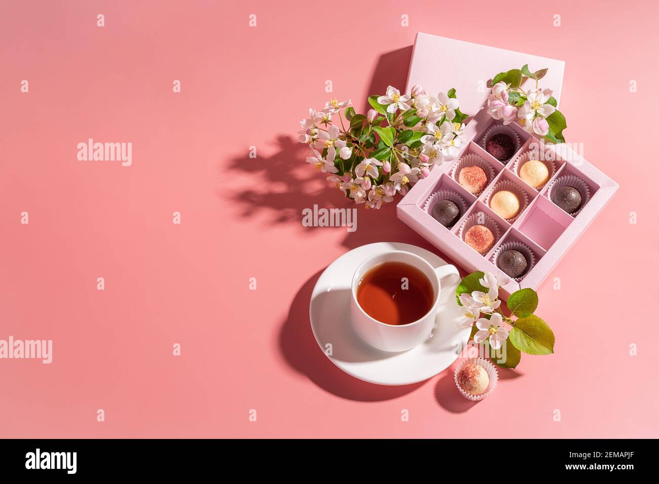 Caramelle al tartufo al cioccolato di vari colori in una elegante scatola  festosa, una tazza di tè su sfondo rosa pastello, decorata con fiori freschi.  Vacanze Foto stock - Alamy