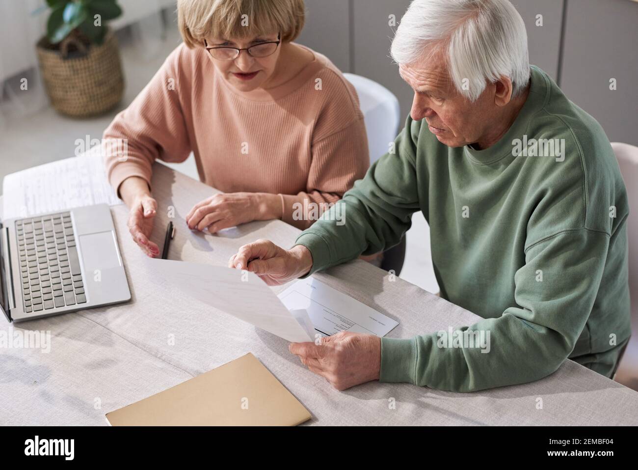 Coppia senior seduta al tavolo con il computer portatile e l'esame documenti finanziari che pagano le fatture per appartamento Foto Stock