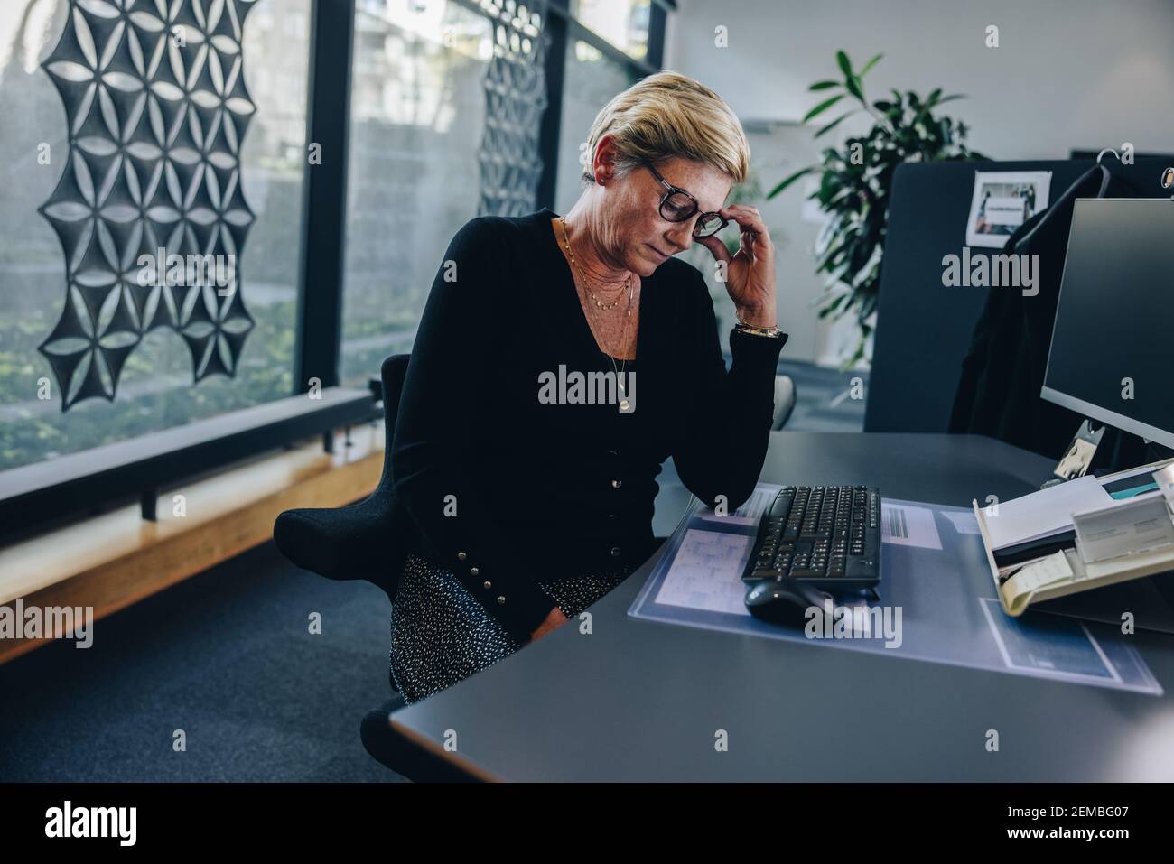 Donna d'affari anziana che guarda stanco seduto alla sua scrivania. La sensazione professionale femminile è stressata mentre si lavora in ufficio. Foto Stock