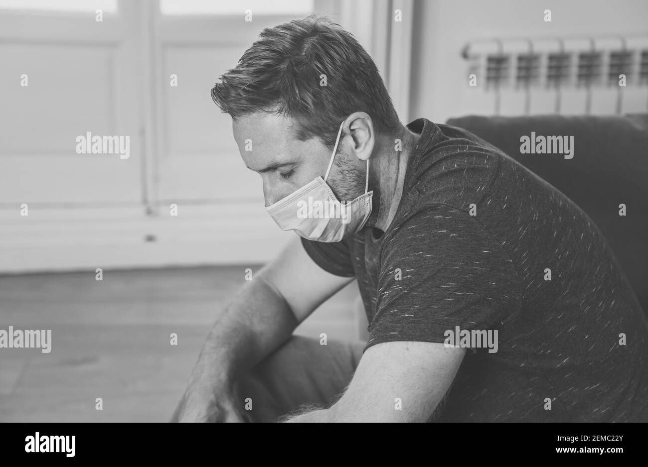 Uomo triste con maschera protettiva sul divano del soggiorno domestico sentirsi stanco e preoccupato soffrendo depressione in mezzo al blocco del coronavirus e distan sociale Foto Stock