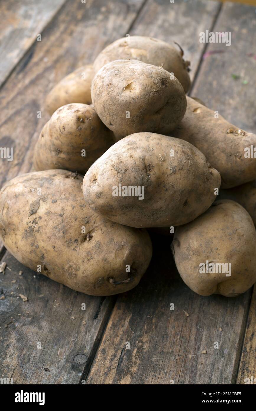 Pila di patate su tavole di legno con un sacchetto di patate sullo sfondo Foto Stock