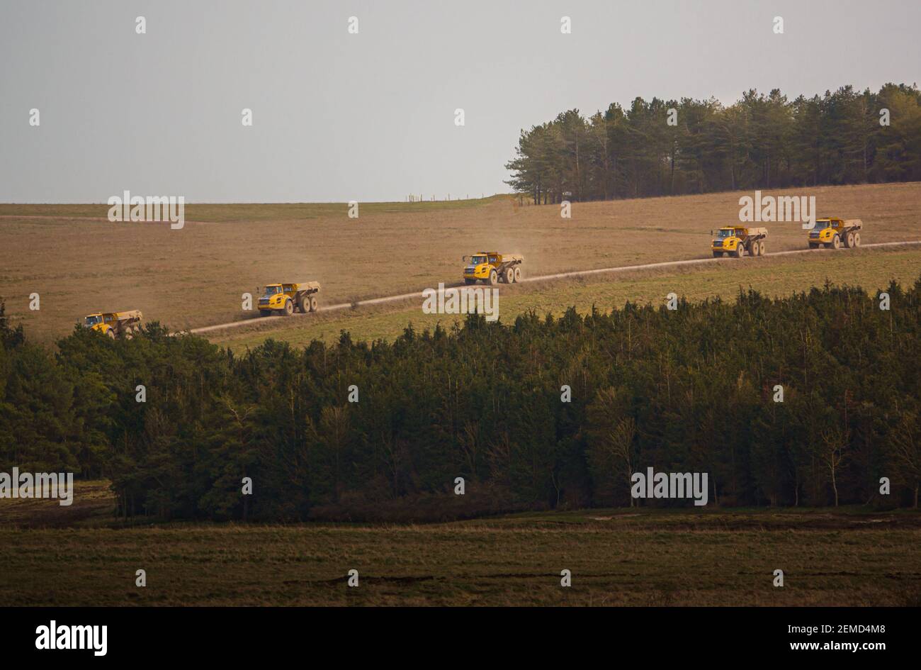 I dumper articolati Yellow Volvo A40E e A40F sparano a terra in un convoglio che fa calciare la polvere mentre attraversano Salisbury Plain, Wiltshire Foto Stock