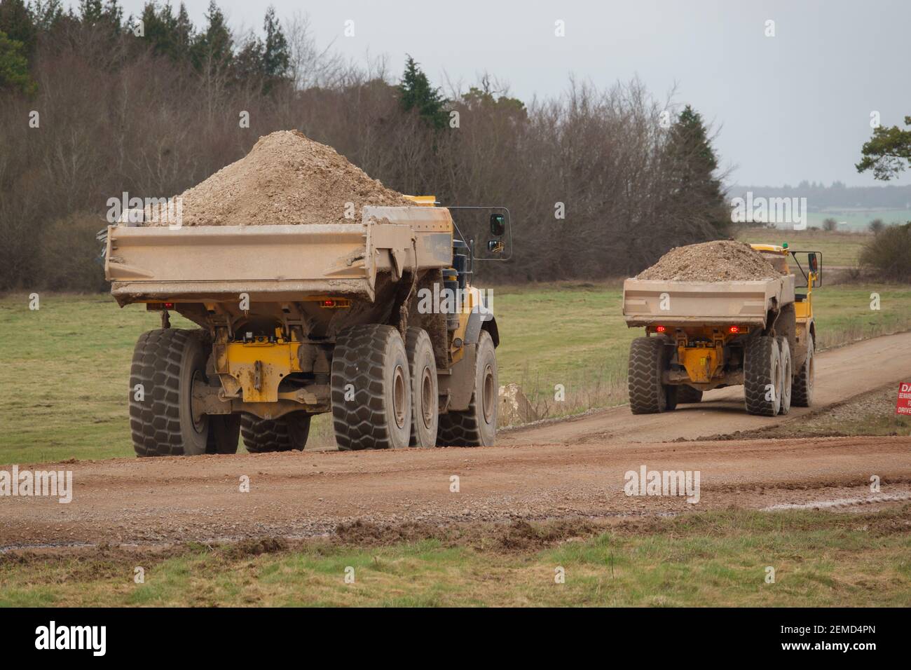 I dumper articolati Yellow Volvo A40E e A40F sparano a terra in un convoglio che fa calciare la polvere mentre attraversano Salisbury Plain, Wiltshire Foto Stock