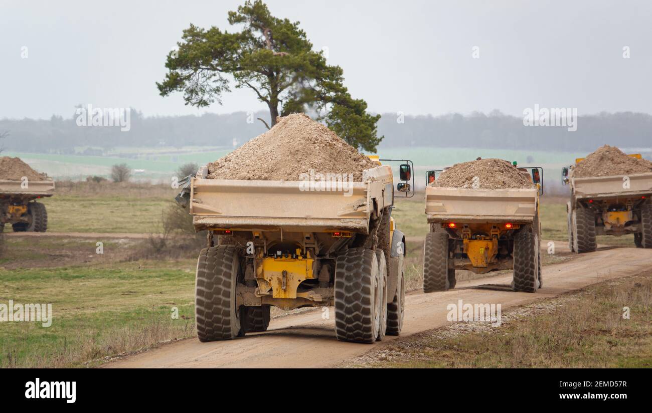 I dumper articolati Yellow Volvo A40E e A40F sparano a terra in un convoglio che fa calciare la polvere mentre attraversano Salisbury Plain, Wiltshire Foto Stock