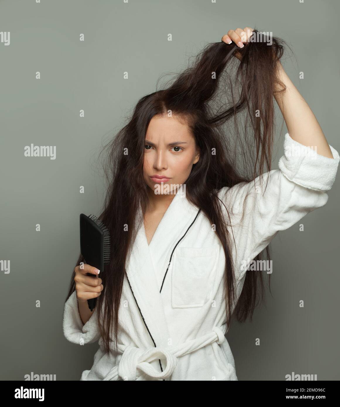 Donna infelice che combatte i suoi capelli aggrovigliati su sfondo bianco, cura dei capelli e concetto di problema dei capelli Foto Stock