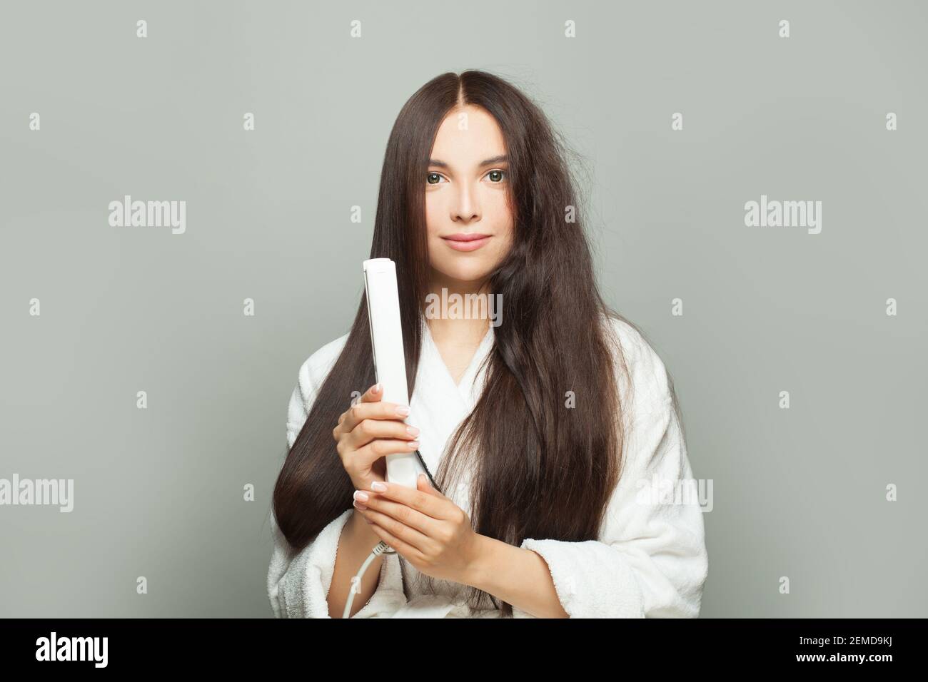 La giovane donna raddrizza i capelli con la piastra su sfondo bianco. Concetto di cura dei capelli Foto Stock