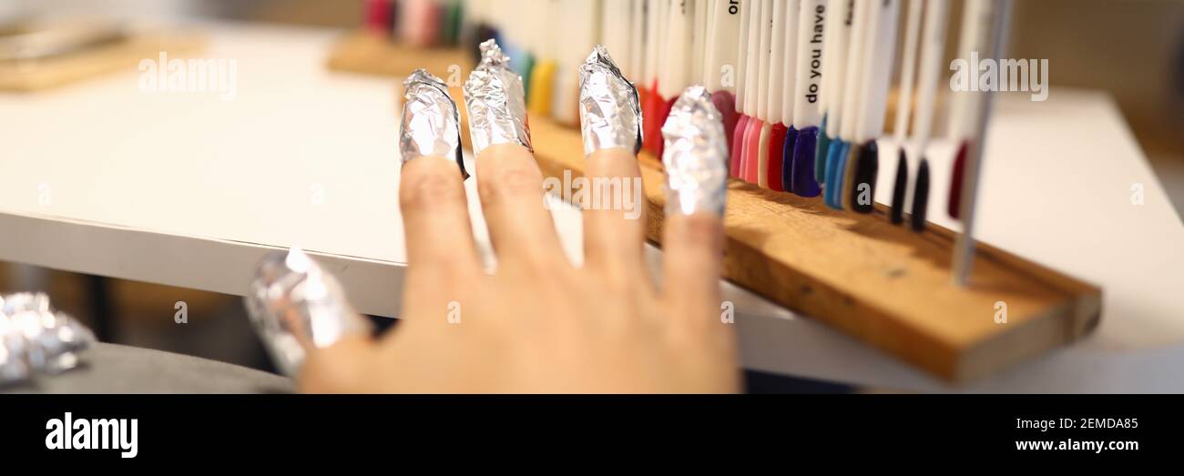 La mano della donna con il foglio sulle unghie è in piedi accanto a campioni di vernice con tavolozza di colori. Foto Stock
