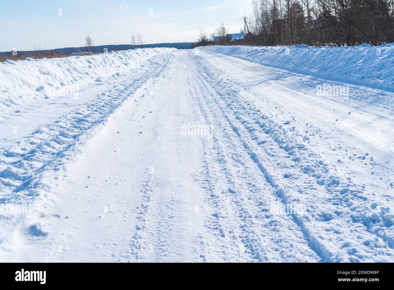 Strada rurale in inverno coperta di neve arrotolata sul sfondo di campi innevati e boschi con un azzurro chiaro cielo Foto Stock