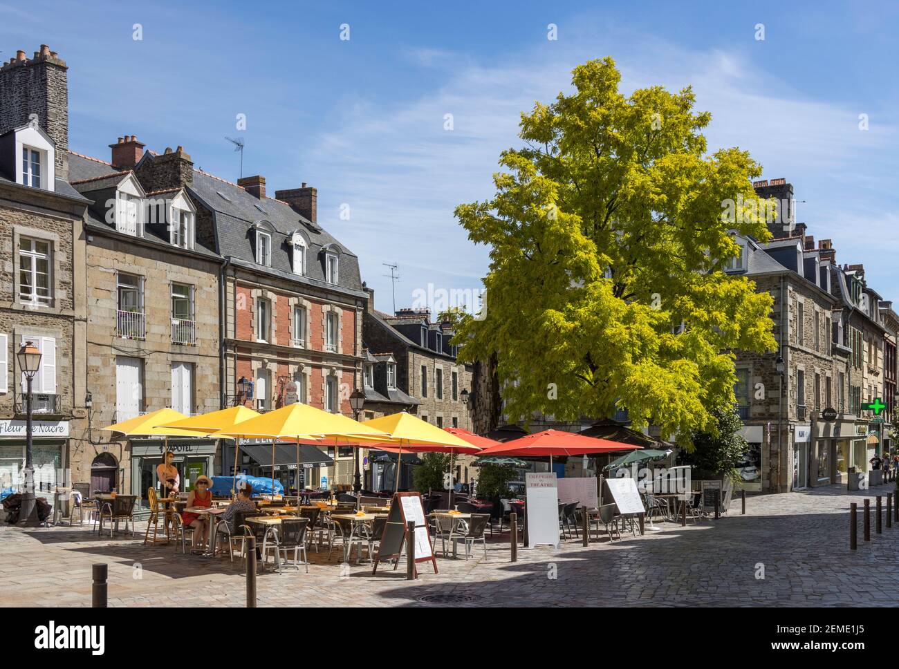 Le persone si rilassano in un caffè all'aperto a Fougeres, in Francia, godendo di un luminoso sole estivo sotto l'ombra di ombrelloni colorati circondati da edifici Foto Stock