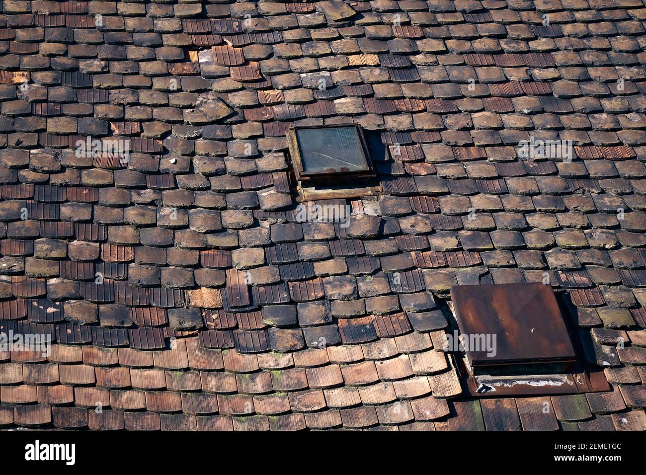 Vecchio tetto, in attesa di ristrutturazione, con tegole in ceramica in cattive condizioni e due lucernari con vetri rotti; foto a colori. Foto Stock