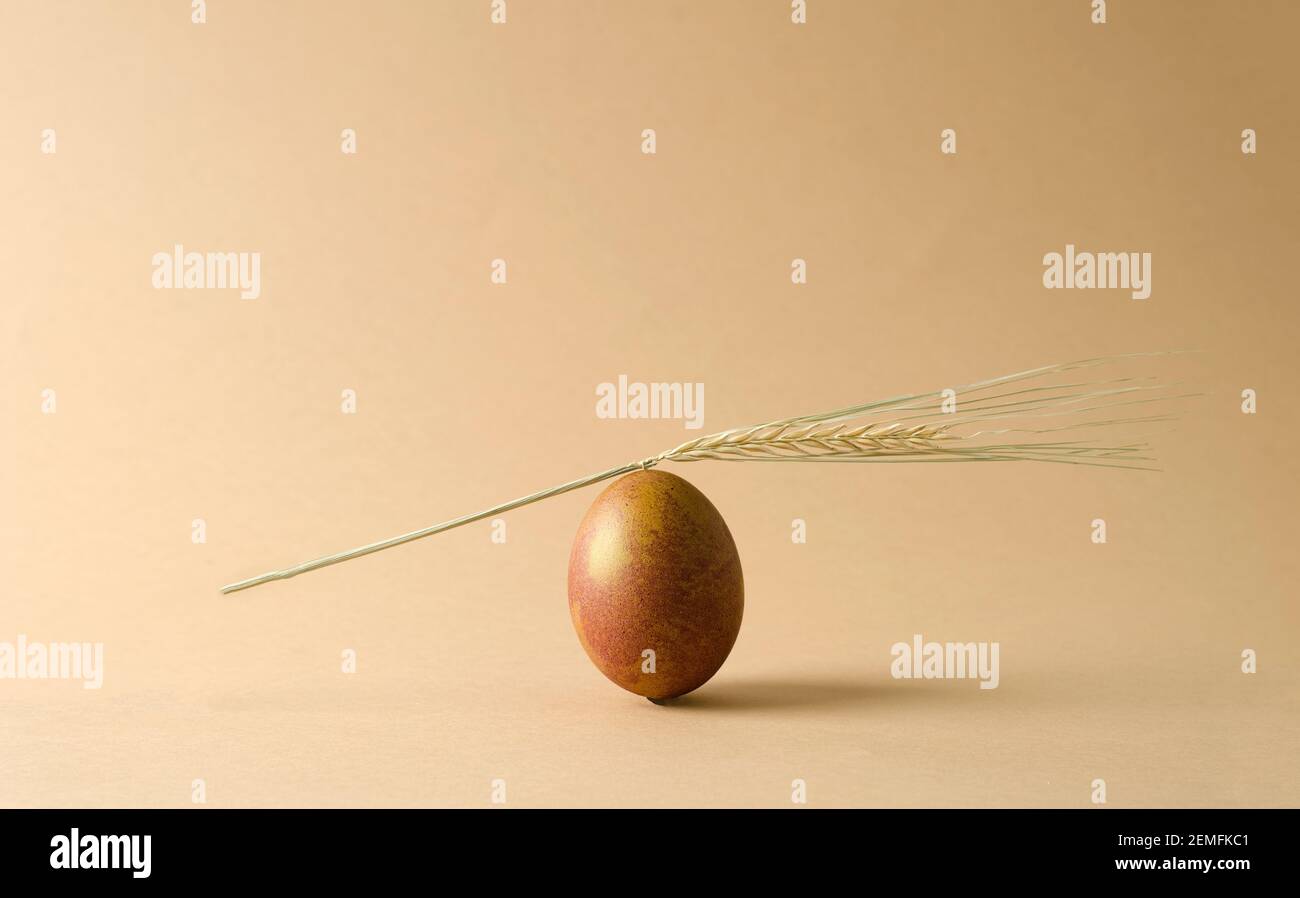 Un uovo di pollo marrone naturale si erge su uno sfondo beige. Un orecchio di grano giace sull'uovo. Minimalismo, monocromatico, concetto sfondo pasquale con copia Foto Stock