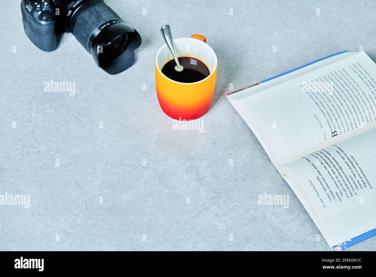Apri il libro, la macchina fotografica e la tazza da caffè con il cucchiaio sul tavolo grigio Foto Stock
