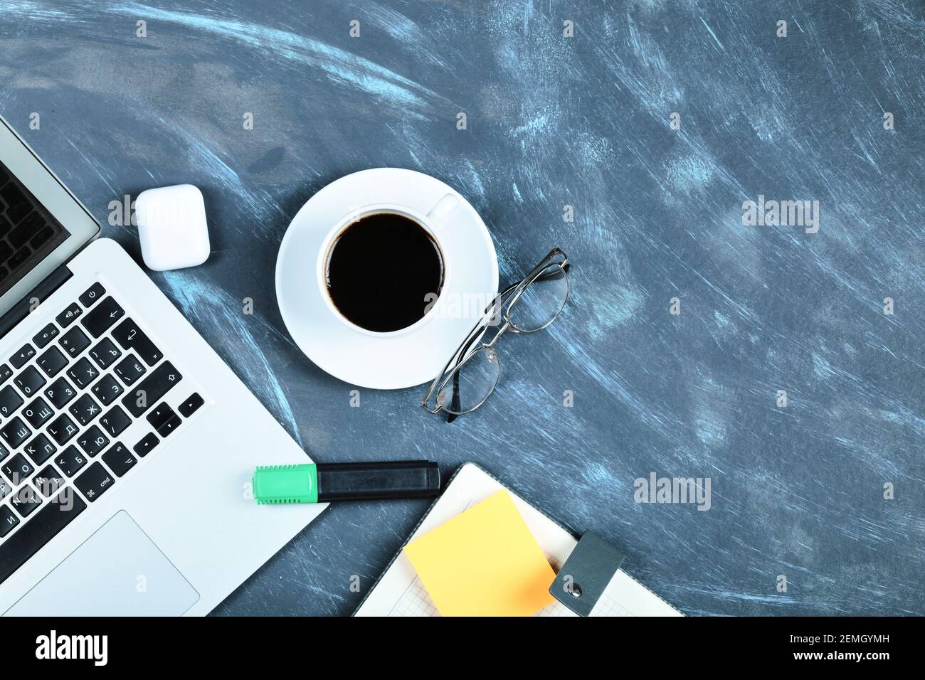 Una tazza di tè, computer portatile, notebook, bicchieri e appunti sulla scrivania blu Foto Stock