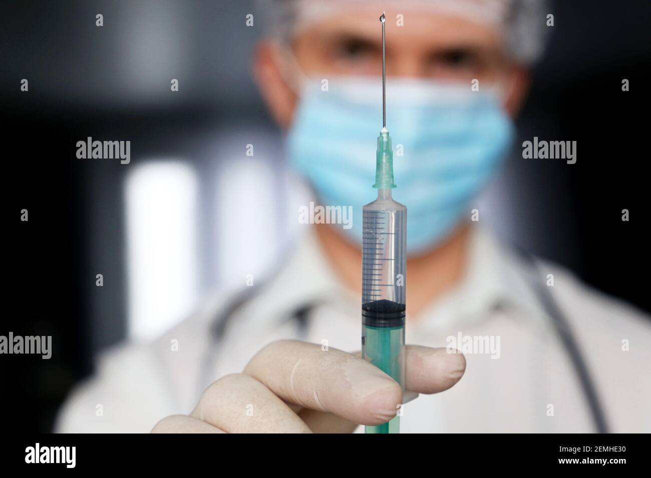 Siringa in mano del medico, uomo in maschera medica e guanti protettivi che si preparano all'iniezione. Concetto di vaccinazione durante la pandemia di covid-19 Foto Stock