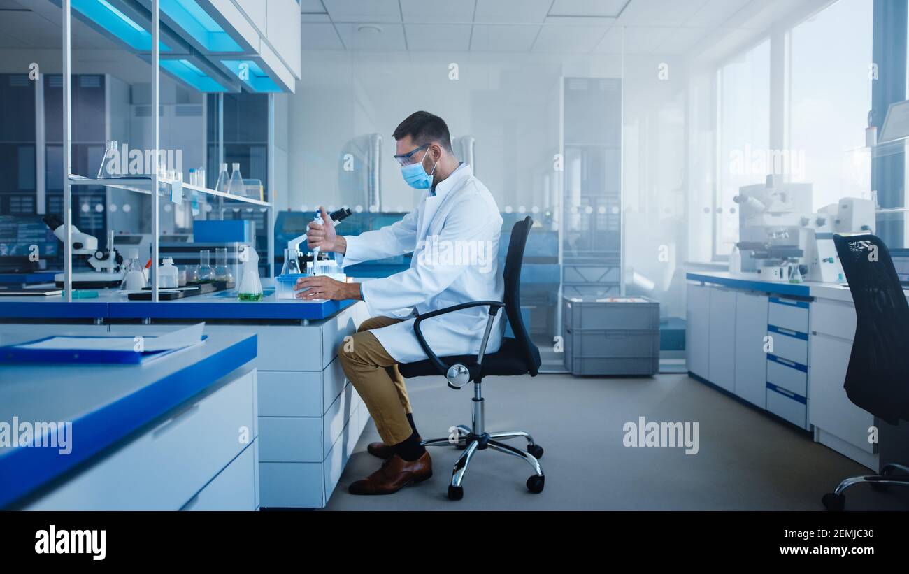 Modern Medical Research Laboratory: Lo scienziato indossa la maschera facciale lavorare con la pipetta, analizzare il campione microbiologico. Advanced Scientific Lab per Foto Stock