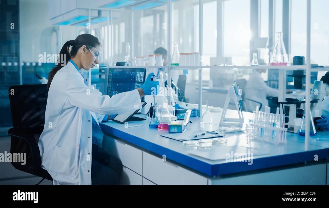 Modern Medical Research Laboratory: Scienziati donne che lavorano con le pipette, utilizzando Digital Tablet, analizzando i campioni biochimici. Medicina scientifica Foto Stock