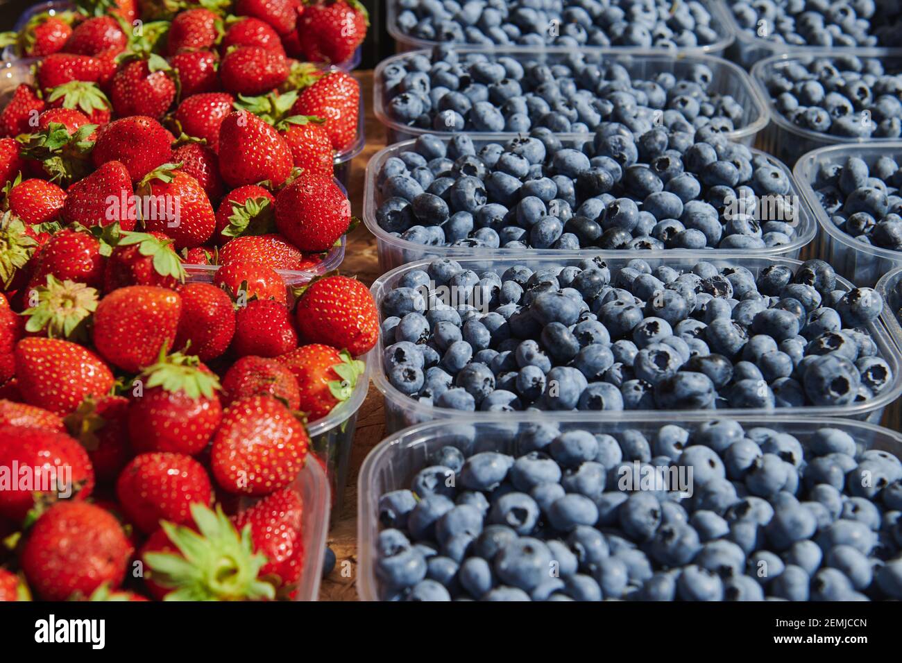 Scatole di plastica con mirtilli e fragole al mercato in una giornata di sole. Prodotti agricoli. Foto Stock