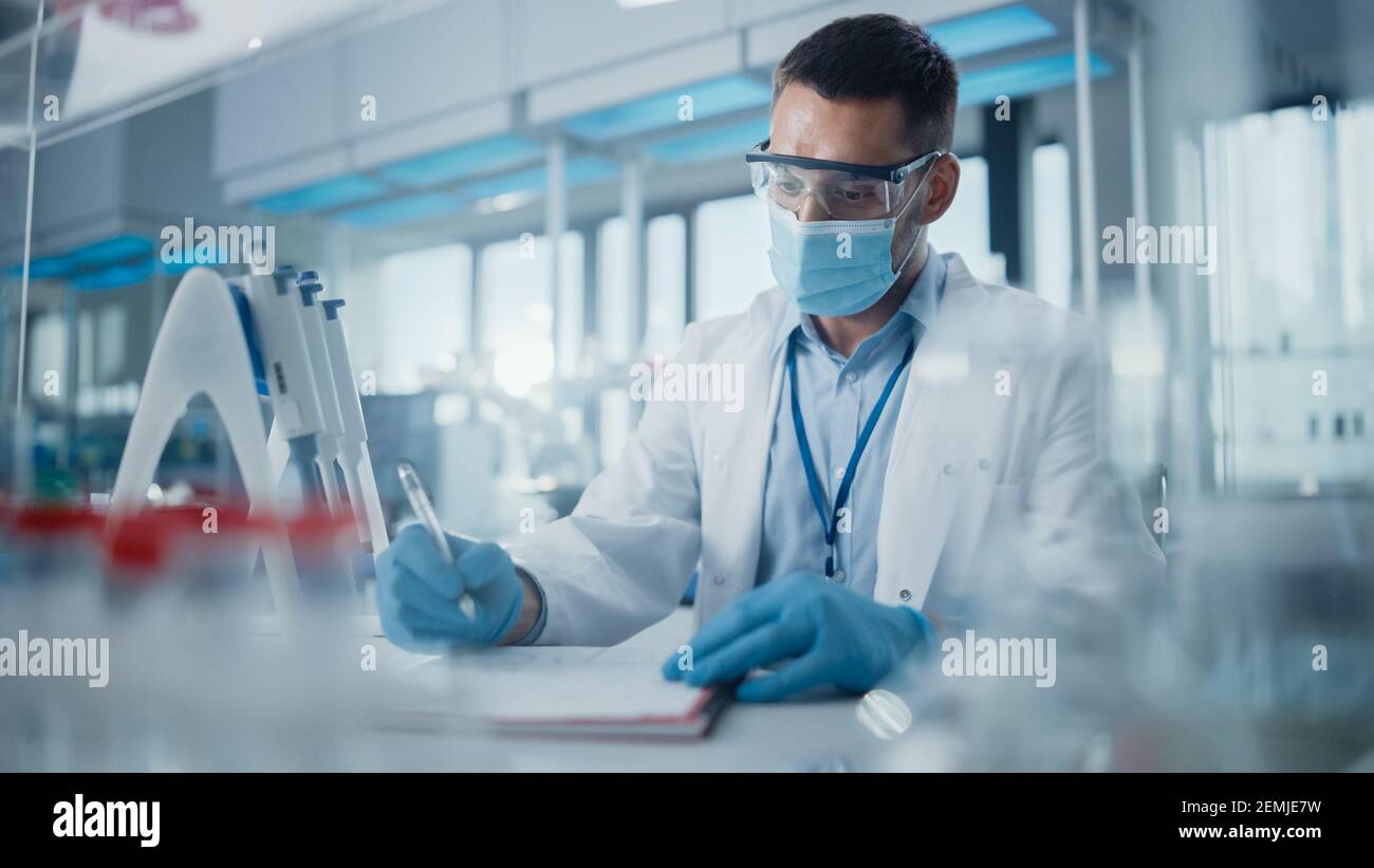 Laboratorio di Ricerca medica: Ritratto dello scienziato che indossa la maschera di faccia che analizza le sostanze biochimiche, scrivendo le informazioni. Advanced Scientific Lab per Foto Stock