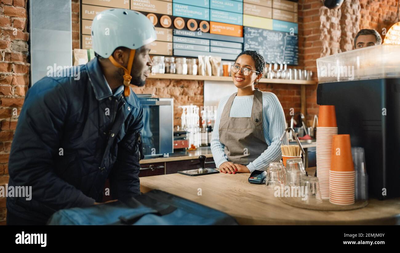 Black African American Food Delivery Courier parla con un giovane barista nel moderno Bright Cafe Restaurant. Il personale era molto vario e felice Foto Stock