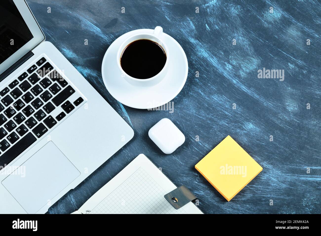 Una tazza di tè, computer portatile, notebook e appunti sulla scrivania blu Foto Stock