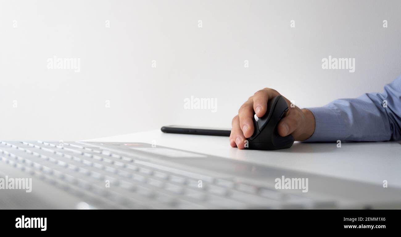 foto panoramica di un mouse verticale con un computer portatile moderno. mano di un uomo in camicia con un mouse verticale ergonomico, realizzato per la prevenzione della carpa Foto Stock