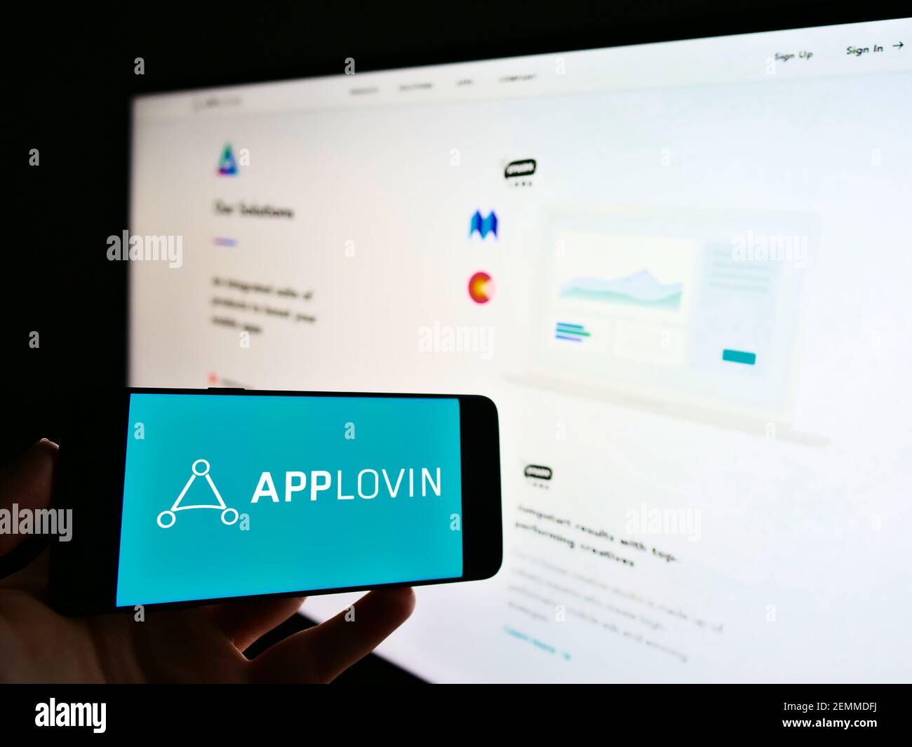 Persona che detiene il cellulare con il logo aziendale della piattaforma di tecnologia mobile statunitense AppLovin Corp. Sullo schermo di fronte alla pagina web. Mettere a fuoco il display del telefono. Foto Stock