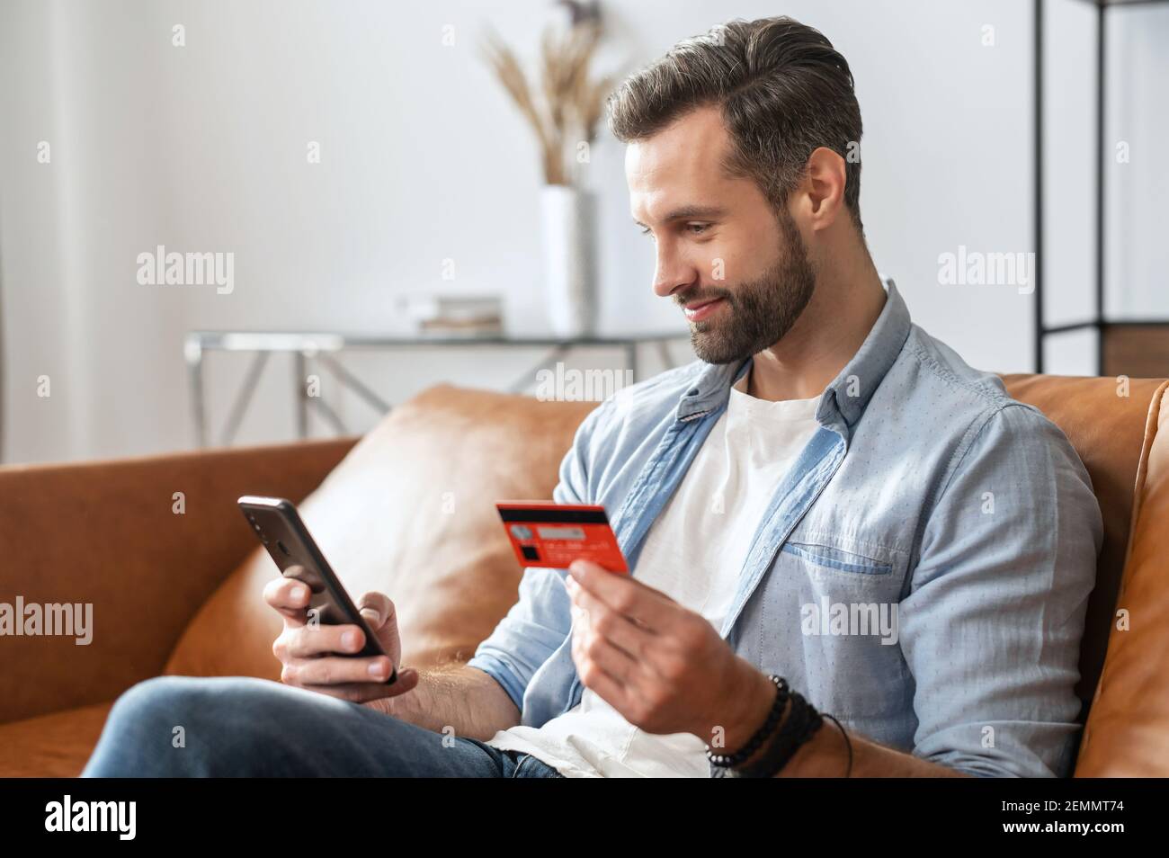 Uomo d'affari hipster bearded, tenendo il telefono cellulare e la carta di credito per lo shopping online e inserendo il numero per effettuare il pagamento, pagare per le utenze, utilizzando un mobile virtuale per gestire il conto bancario Foto Stock