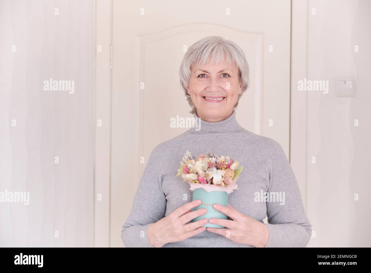 Un ritratto di una donna caucasica anziana sorridente con capelli grigi corti che tiene un bouquet di fiori secchi. Foto Stock