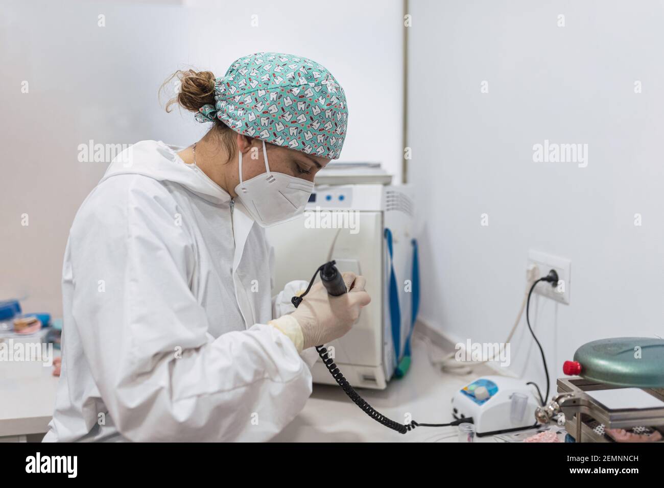 Mani di un tecnico dentale con maschera chirurgica e vetri che lucidano le protesi sulla sua tabella. Concetto di salute Foto Stock